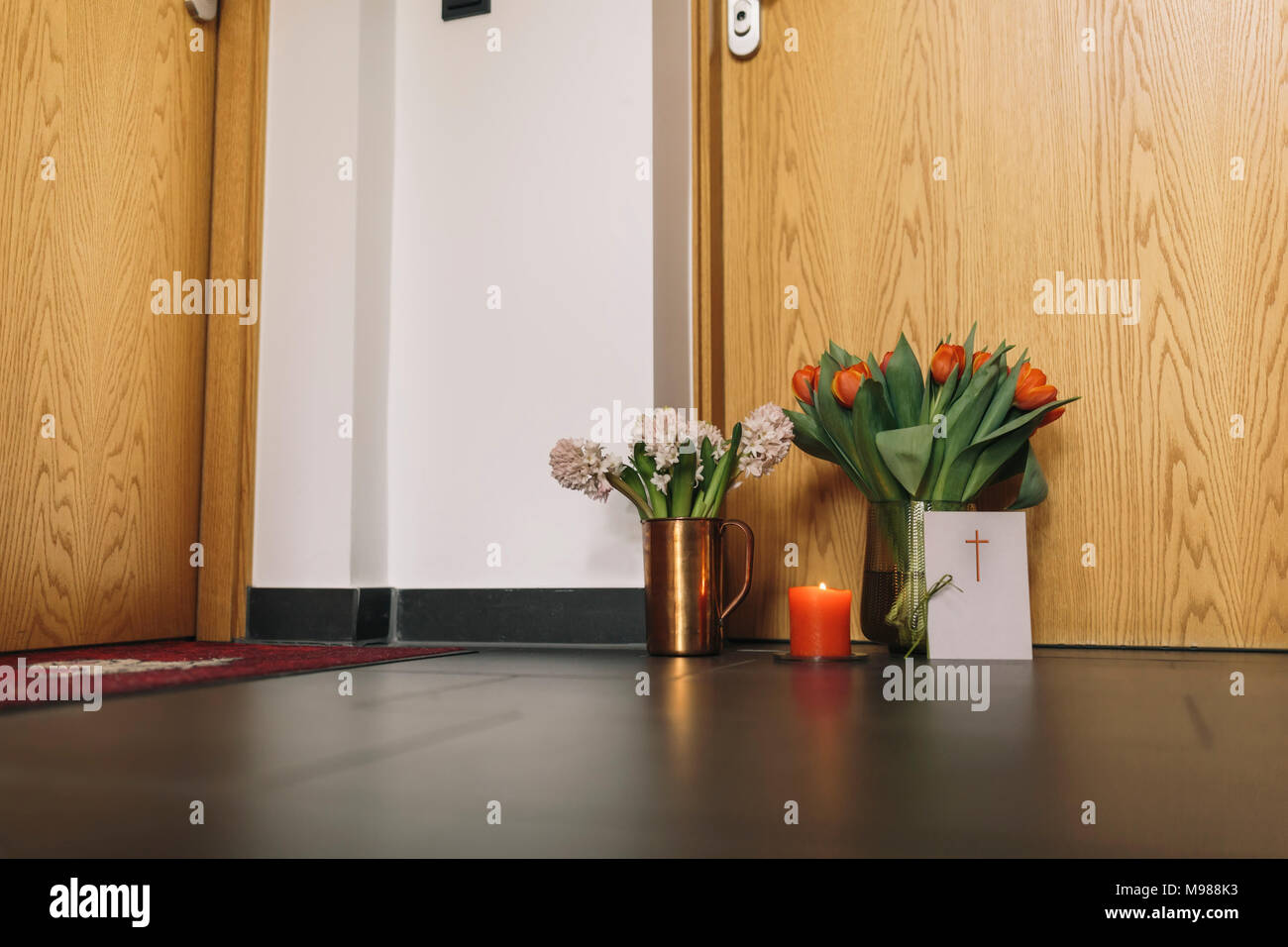 Farewell flowers, candle and condolende card at apartment door of deceased neighbour Stock Photo