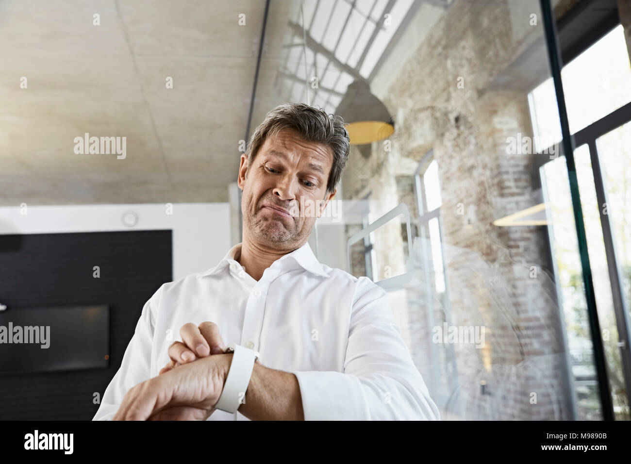 Sceptical businessman in office using smartwatch Stock Photo