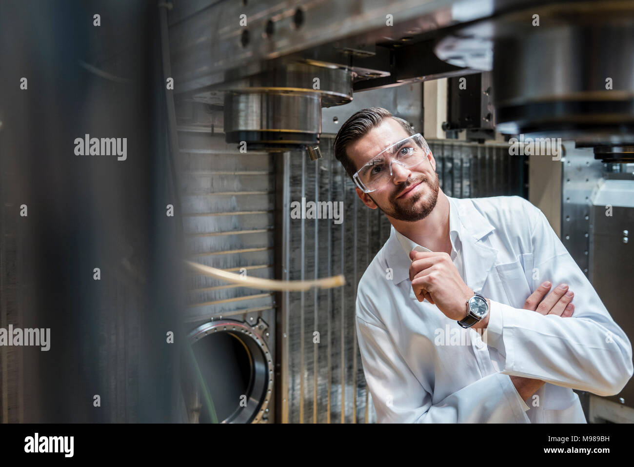 Man wearing lab coat and safety goggles at machine Stock Photo