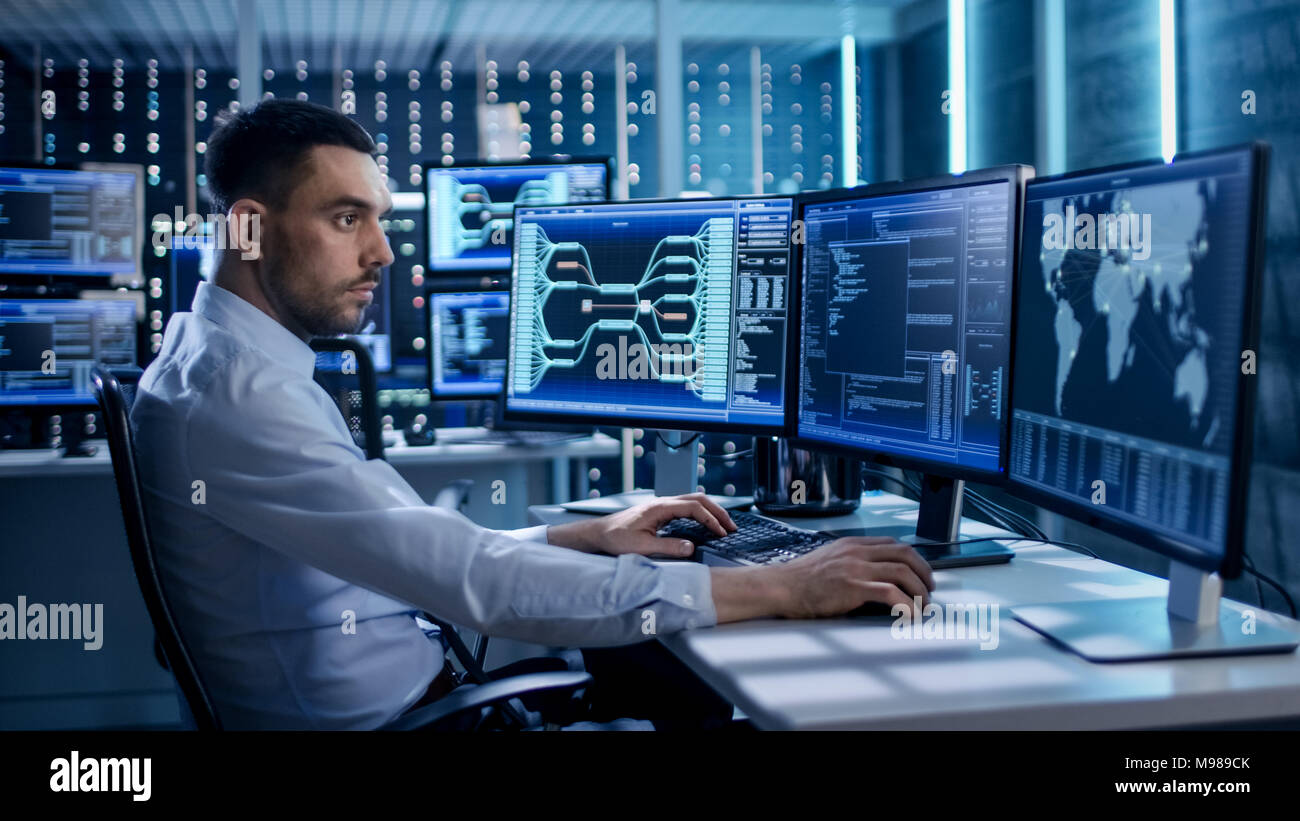 System Security Specialist Working at System Control Center. Room is Full of Screens Displaying Various Information. Stock Photo
