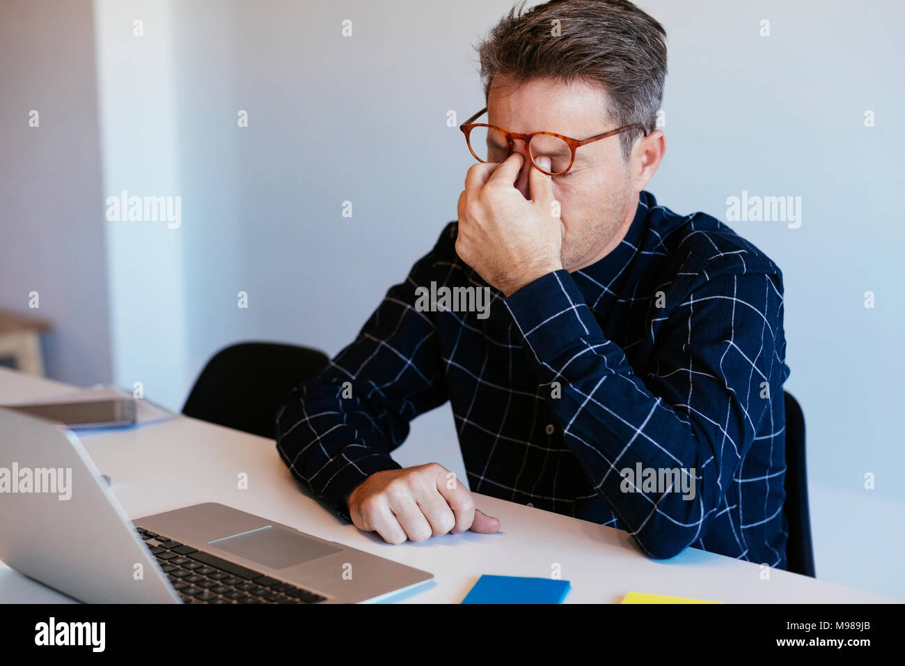 Businessman at desk in office rubbing his eyes Stock Photo