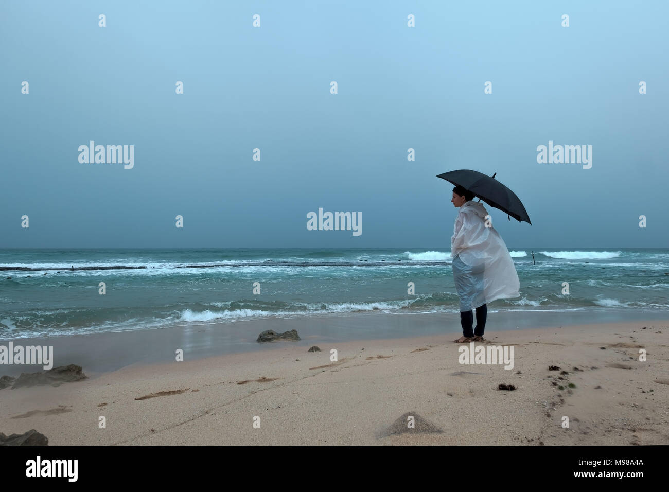 Young woman walking with an umbrella in front of ocean in rainy weather. Enjoy rain in vacation Stock Photo