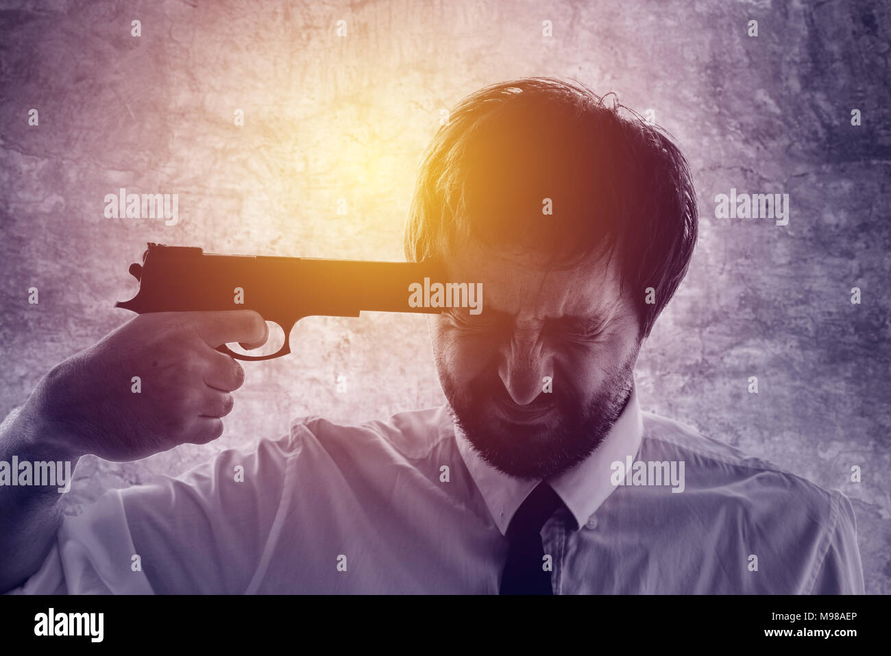 Businessman points gun to his head, disappointed suicidal man about to commit a suicide. Unemployment and business failure concept, ultra violet toned Stock Photo