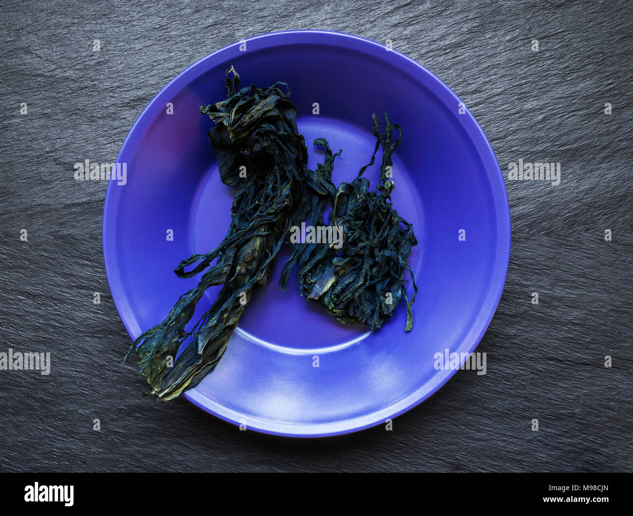 Dry bunch of seaweed in purple plate on black stone surface background Stock Photo