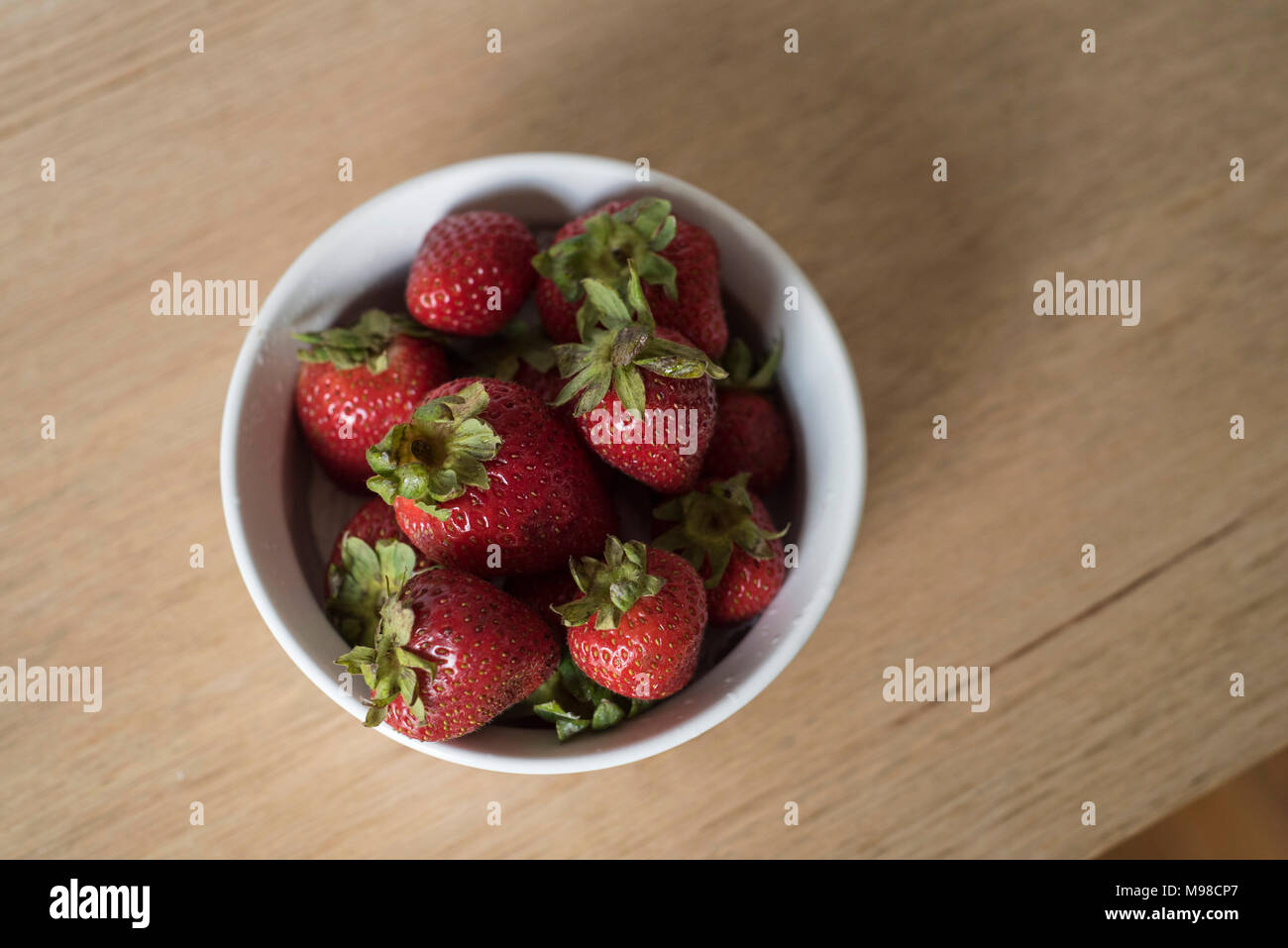 Overhead Shot of Strawberries in White Bowl on a Light Wood Table Top Stock Photo