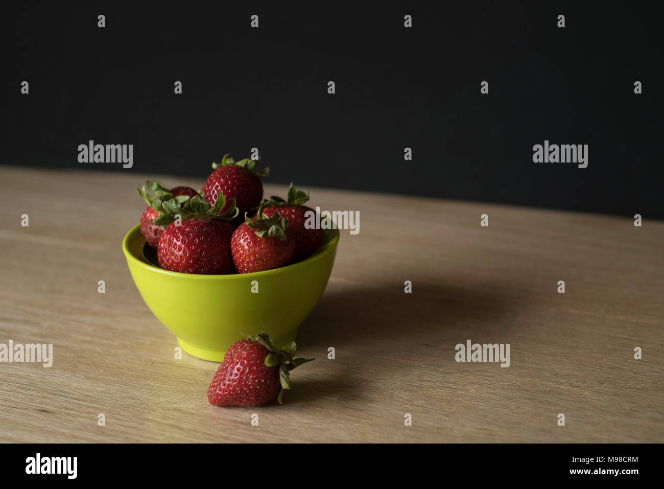 Small Bowl of Strawberries on Counter in Front of Dark Wall Stock Photo