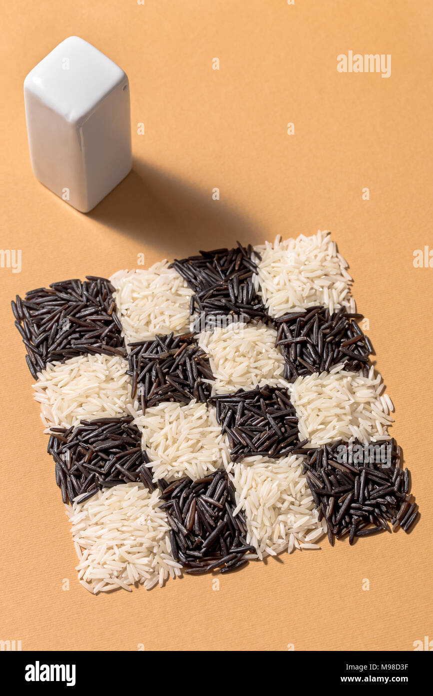Black and white rice in a checkerboard pattern with and rectangular salt shaker on orange background Stock Photo