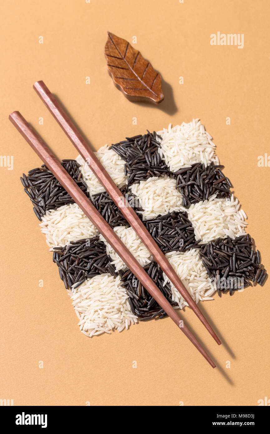 Black and white rice in a checkerboard pattern with chopsticks on vibrant orange background Stock Photo