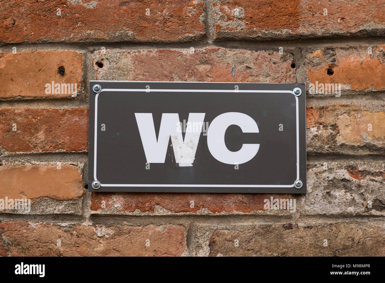 Toilet WC sign on old red brick wall. White WC sign on black metal plate. Outdoor sign. Stock Photo