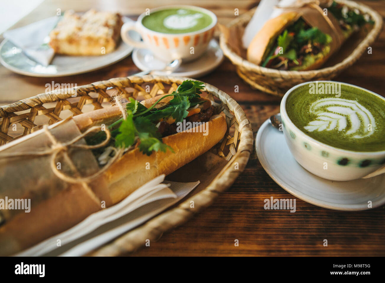 Healthy breakfast: cup of green tea with milk called Matcha, dessert and sandwiches with vegetables and herbs on wooden table Stock Photo