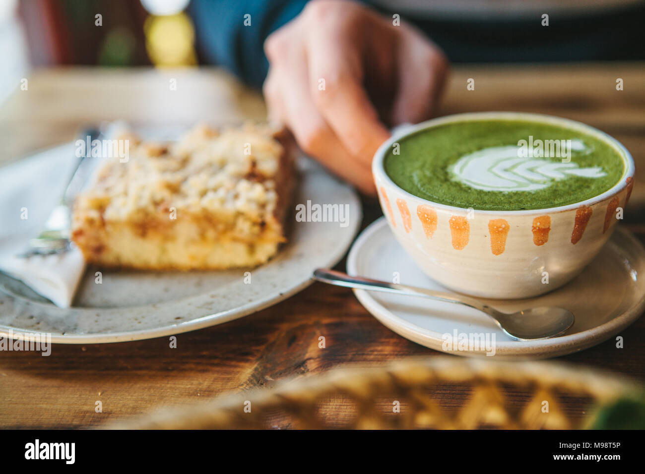 Close-up - man's hand holding mug of green tea with beautiful pattern in the form of white foam next to dessert Stock Photo