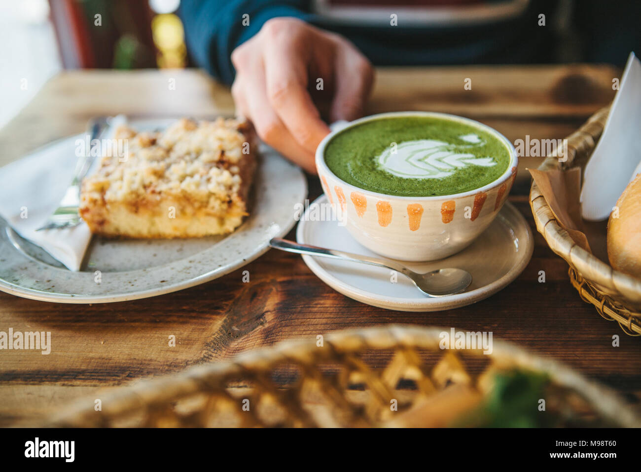 Close-up - man's hand holding mug of green tea with beautiful pattern in the form of white foam next to dessert Stock Photo