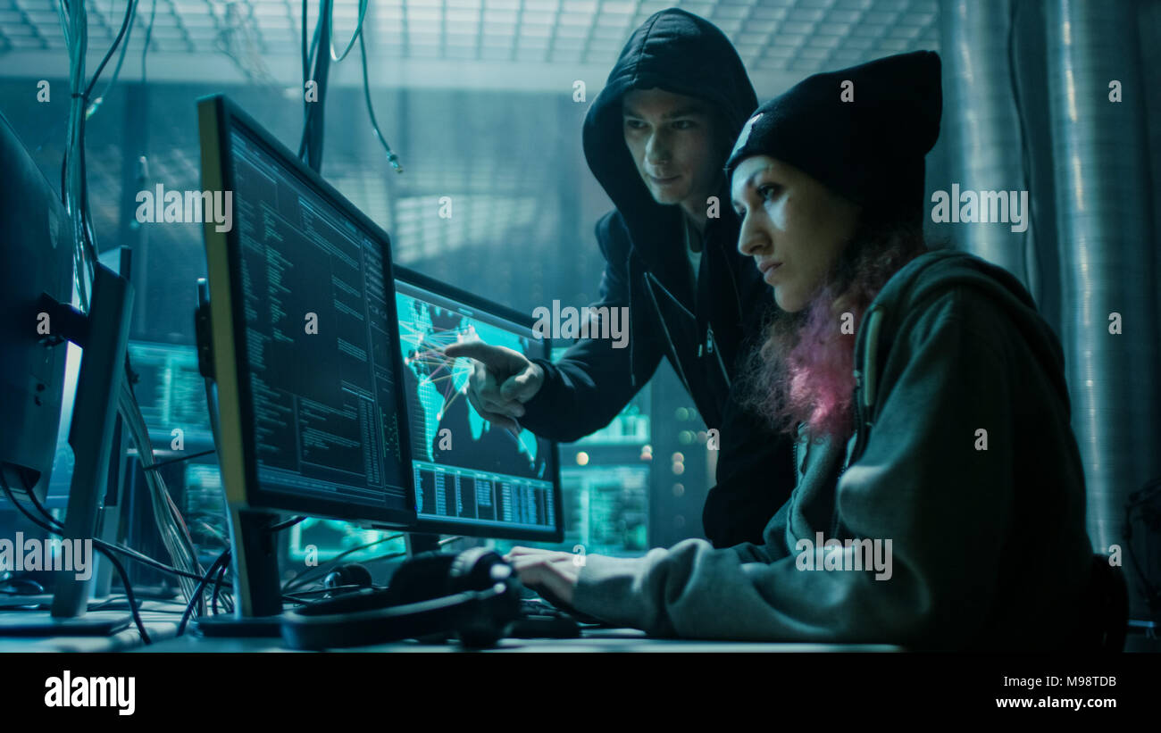 Team of Boy and Girl Hackers Organize Advanced Virus Attack on Corporate Servers. They Work Together. Place is Dark and Has Multiple displays. Stock Photo