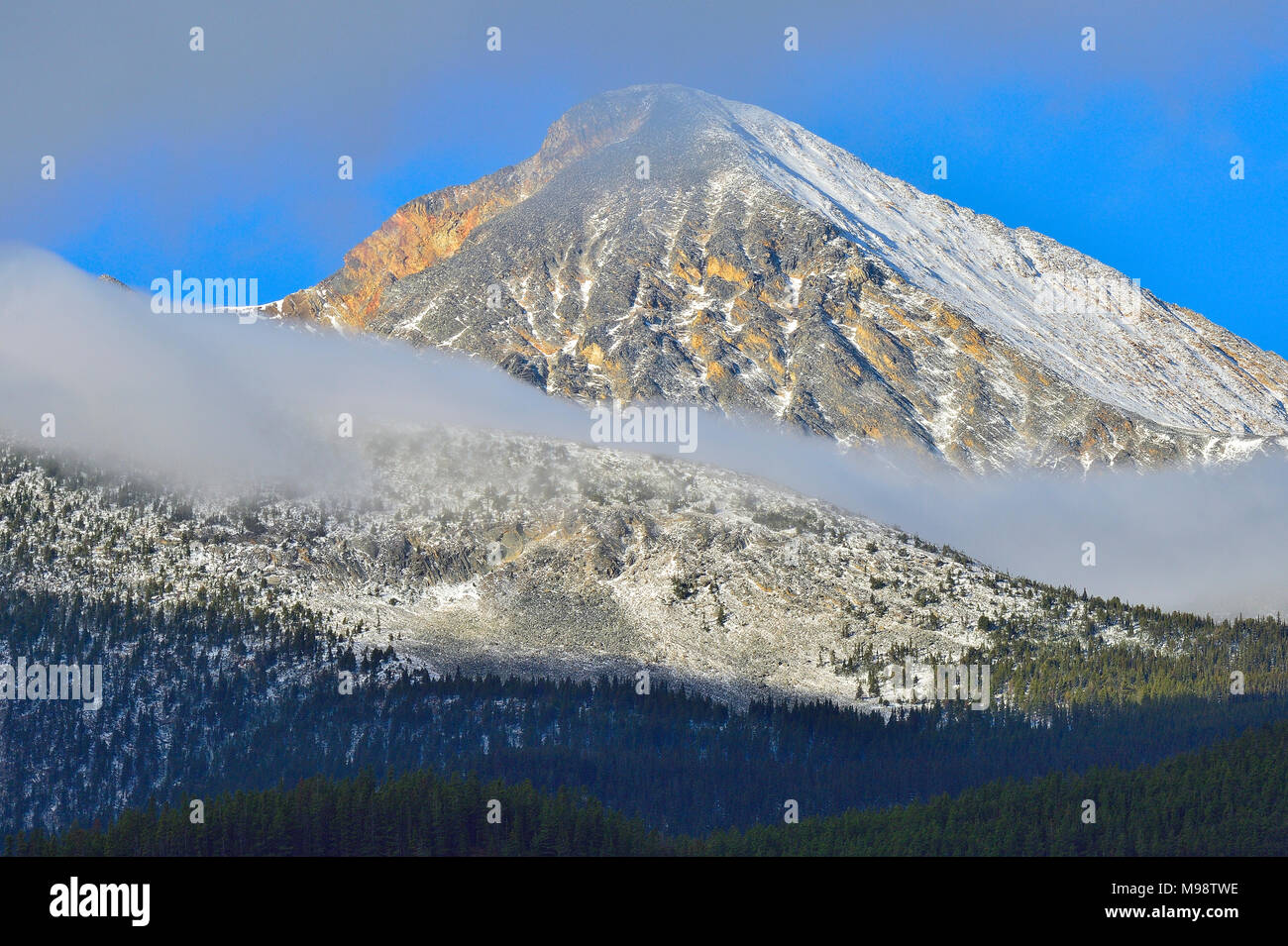 A tall mountain in Jasper National Park stands with wisps of cloud around it on a bright autumn day Stock Photo