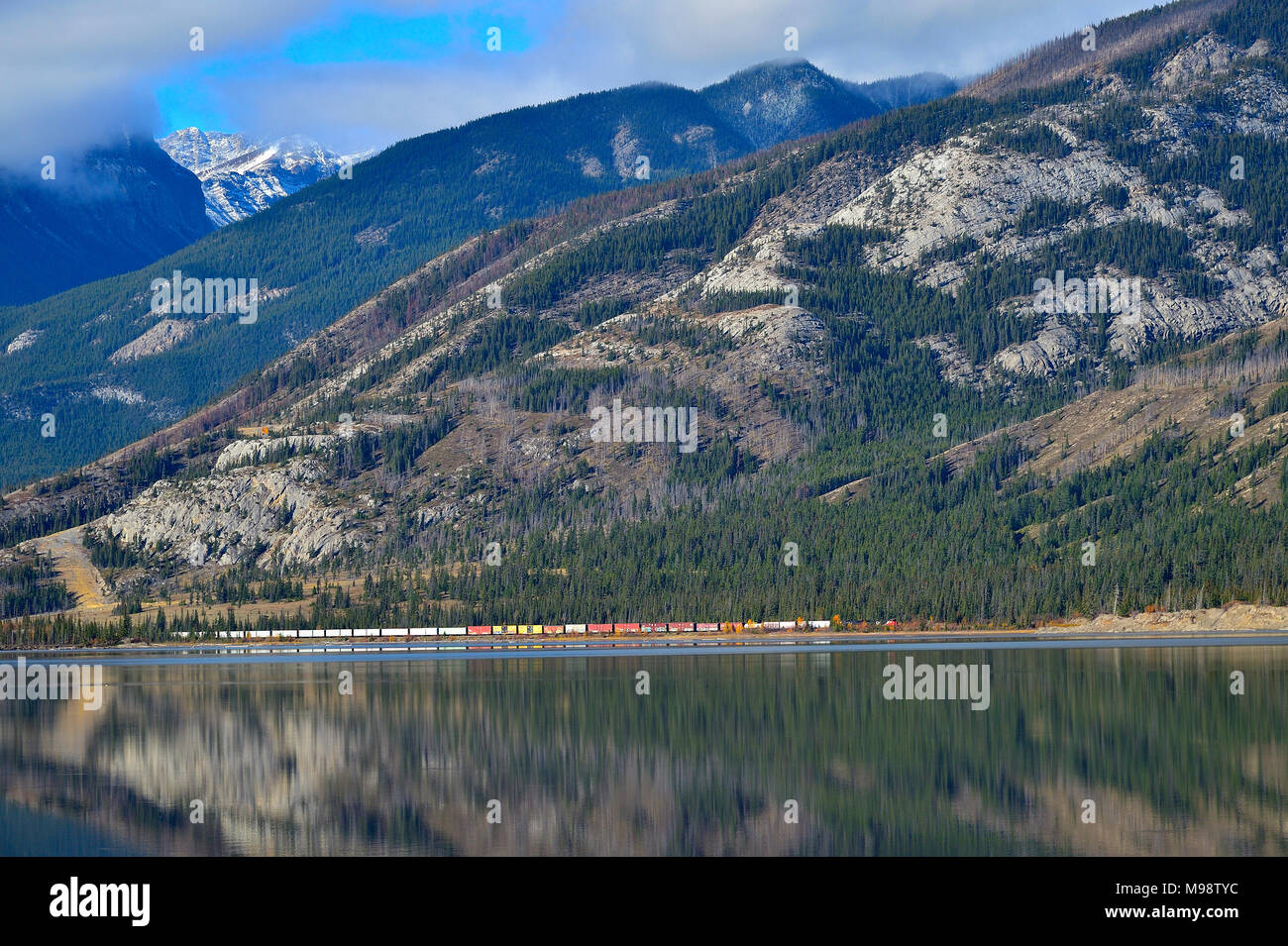 A horizontal image of the rocky mountains along Jasper Lake with a Canadian National freight train rolling along the lakeside in Jasper National Park  Stock Photo
