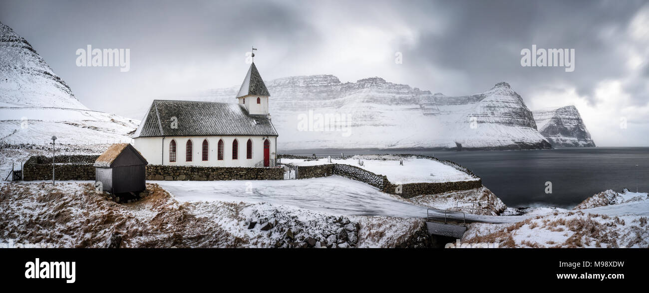 White church in snowy Vidareidi village with Bordoy and Kunoy islands in background, Faroe Islands Stock Photo