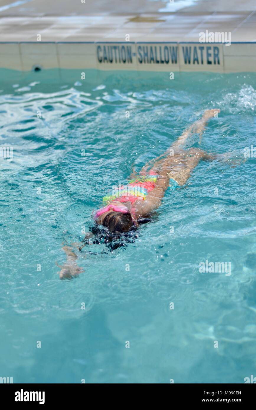Young girl swimming backstroke in a public pool, training, Kokoda