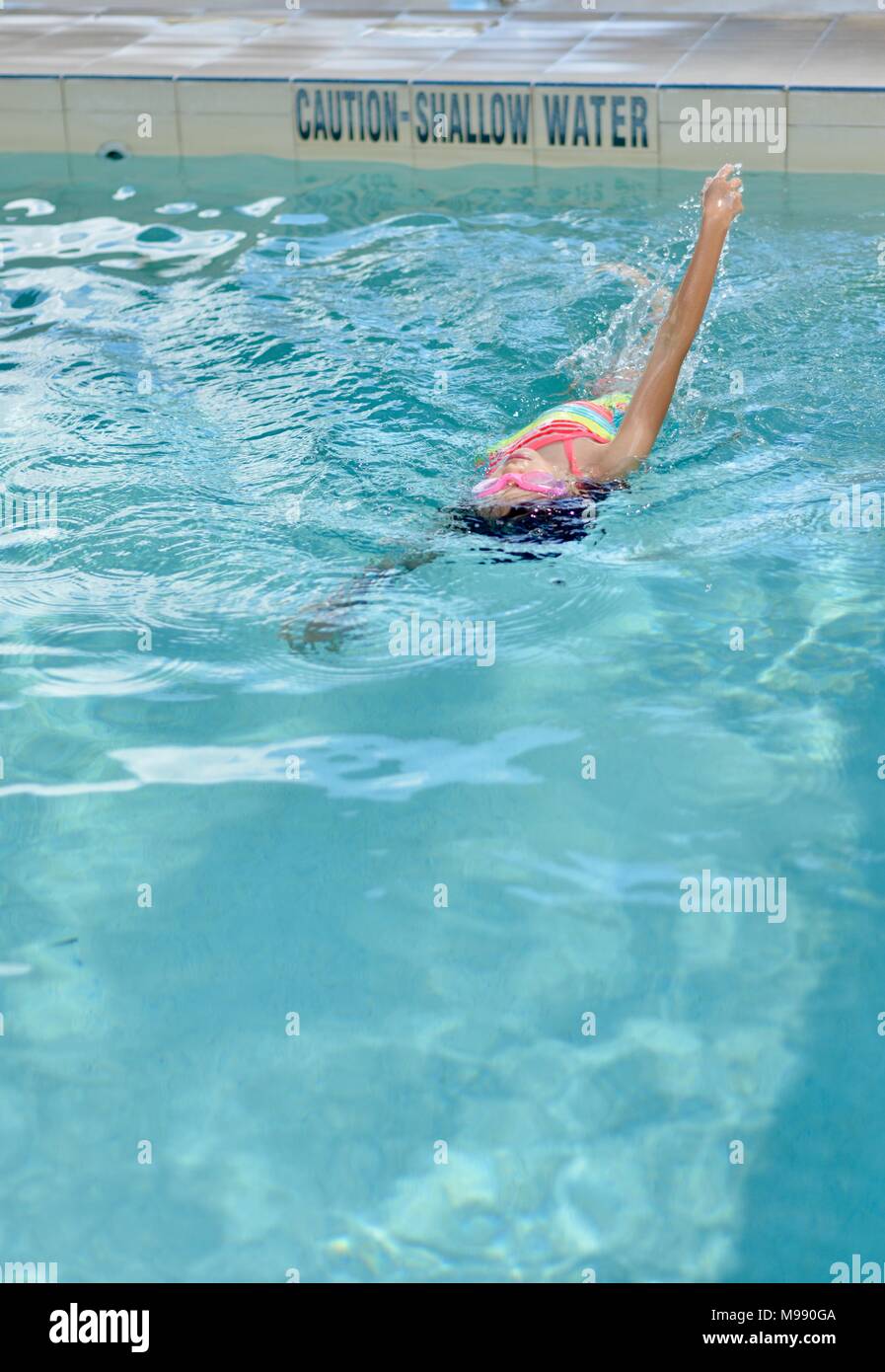 Young girl swimming backstroke in a public pool, training, Kokoda