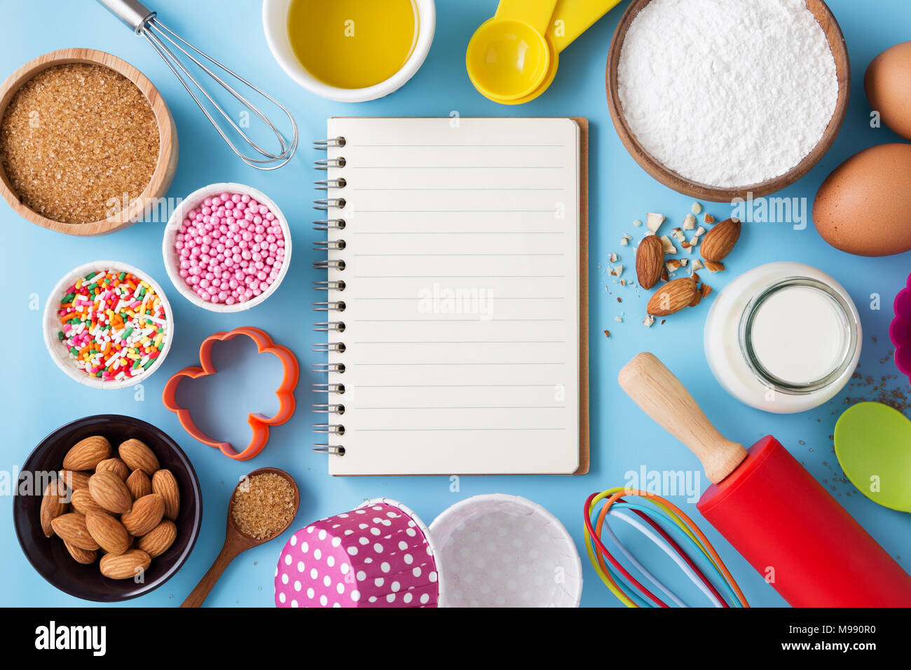 Baking ingredients and utensils with blank recipe book on blue