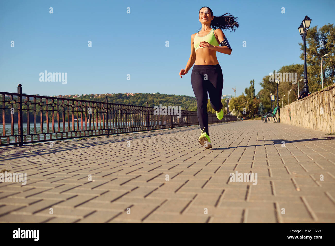 A sports girl runs through the park by the lake. View from behind the woman's jogging. Stock Photo