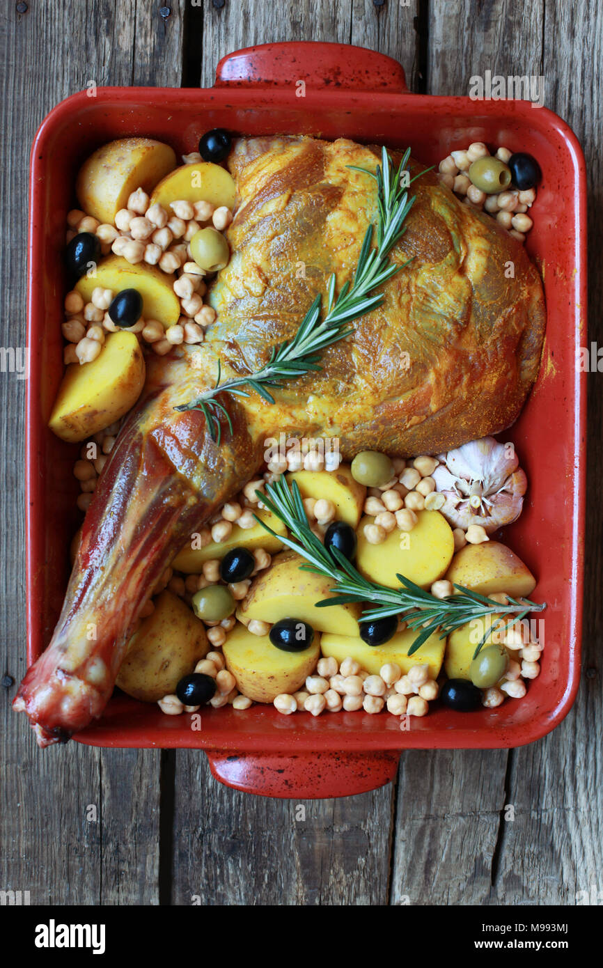 Raw lamb's shoulder blade in roasting dish with potatoes, rosemary
