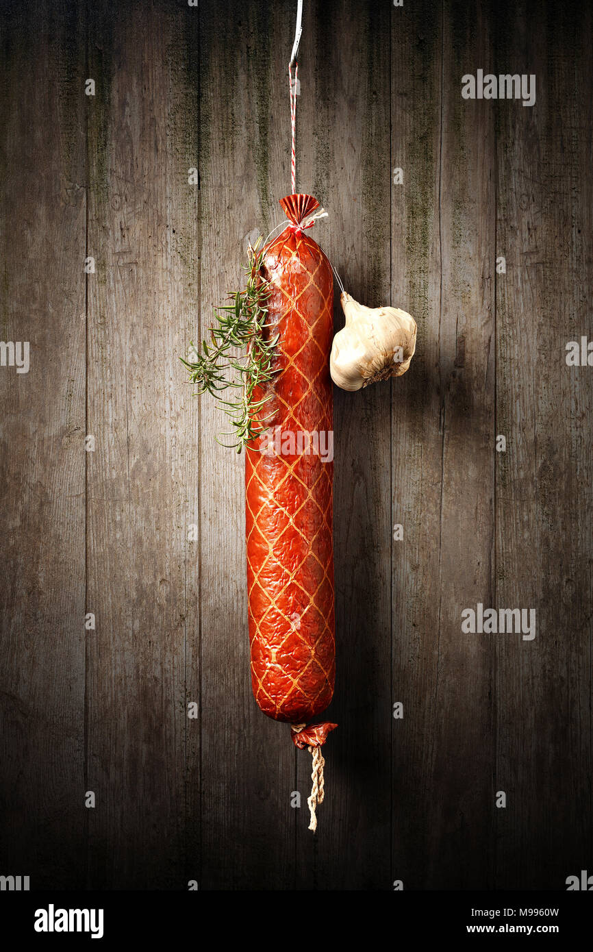 Salami Sausage hanged to dry with Garlic and Rosemary against an old rustic wooden wall Stock Photo