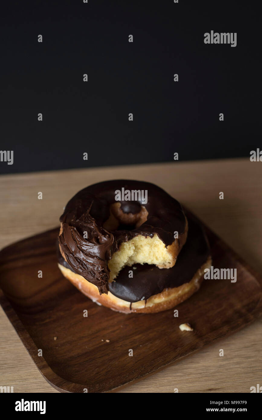 Chocolate Iced Doughnuts with a Bite Missing in front of a Dark Background Stock Photo