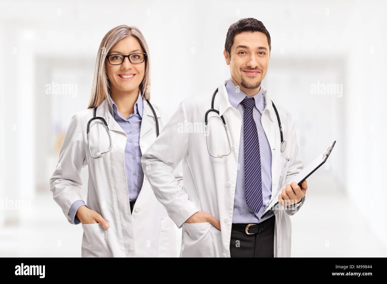 Female doctor and a male doctor with a clipboard looking at the camera and smiling Stock Photo