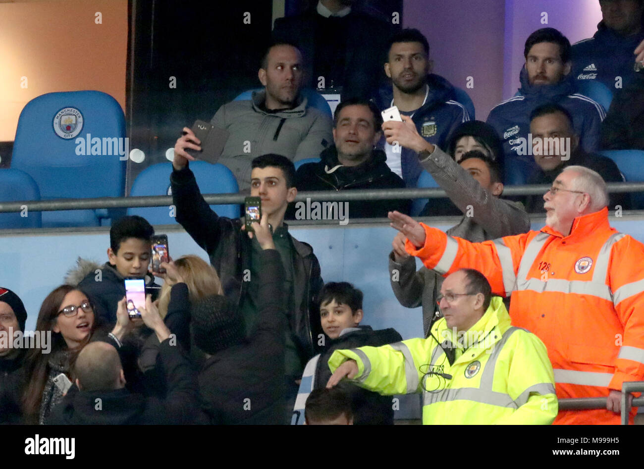 Fans in the stands take photos of Lionel Messi and Sergio Aguero as stewards attempt to stop them during the international friendly match at the Etihad Stadium, Manchester. Stock Photo