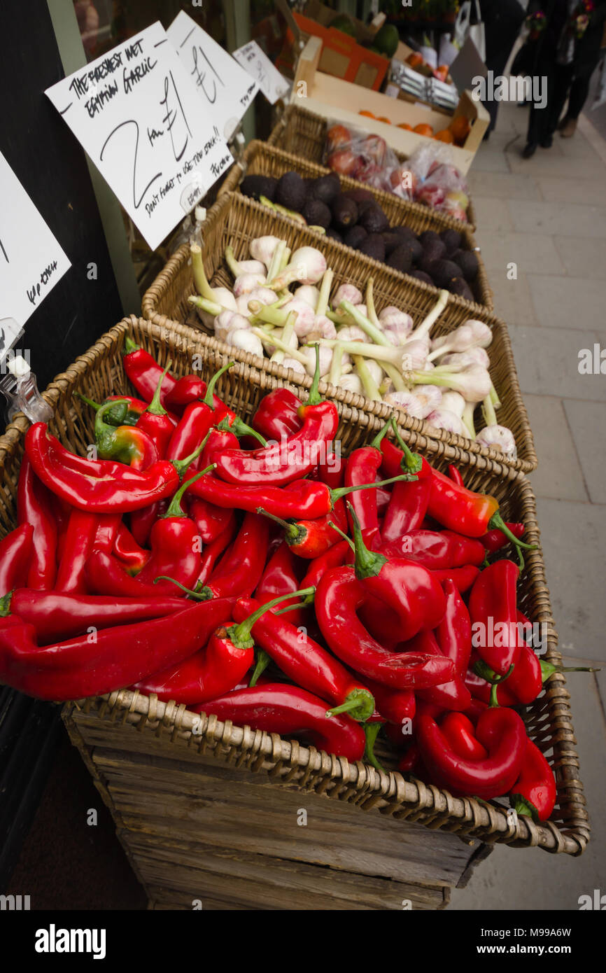 Colourful show of bright red chillies, garlic and avocados on a pavement display outside an independent green grocers shop in the UK Stock Photo