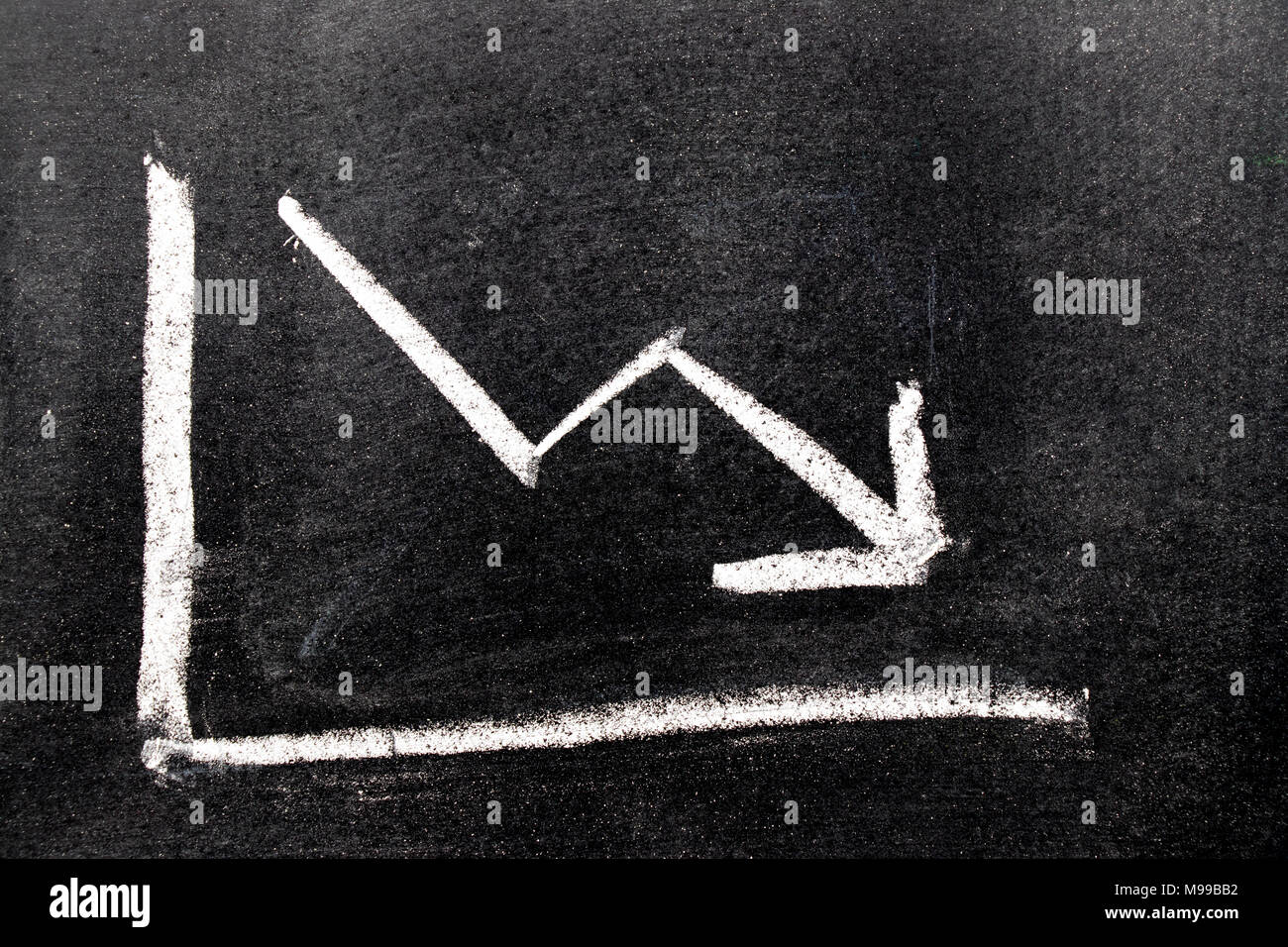 chalk board with sketch of decreasing business graph... White color hand drawing chalk in arrow down shape on black board ...