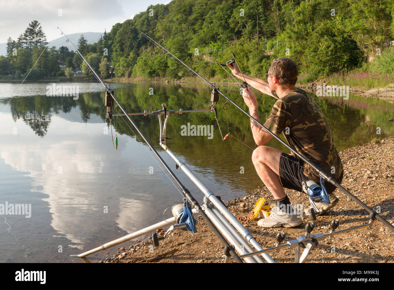 Fishing adventures, carp fishing. Angler with camouflage t-shirt is feeding  fishes throwing boilies with a slingshot Stock Photo - Alamy