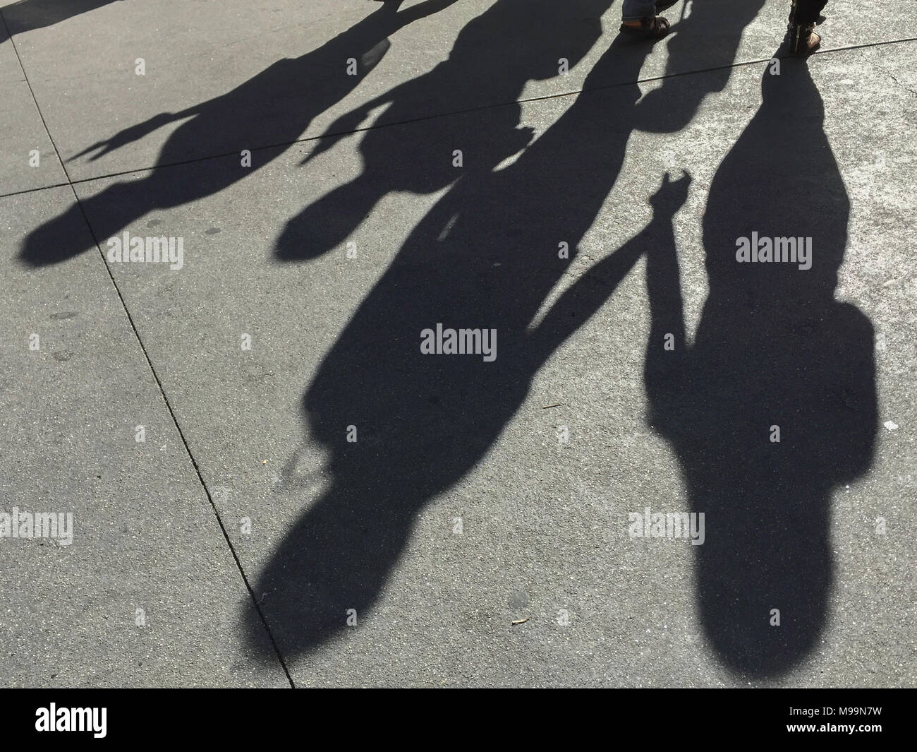 long shadows of people holding hands together and walking along the sidewalk in the afternoon Stock Photo