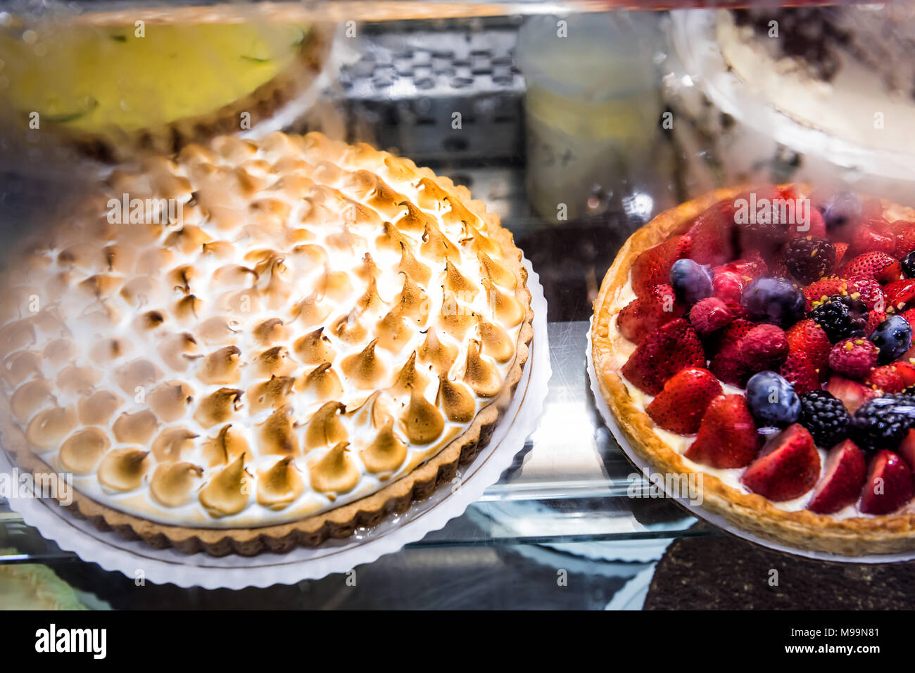 Many cakes on display in bakery shop store with lemon cream meringue, blueberry berry strawberry tart decorations whipped cream, egg whites caramelize Stock Photo