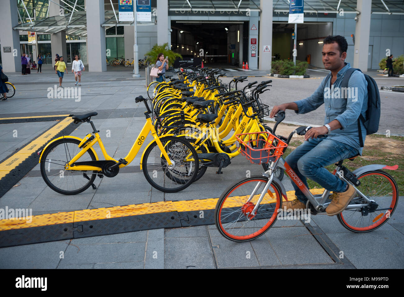22.03.2018, Singapore, Republic of Singapore, Asia - A man rides on his rental  bicycle past parked rental bikes in Marina Bay Stock Photo - Alamy
