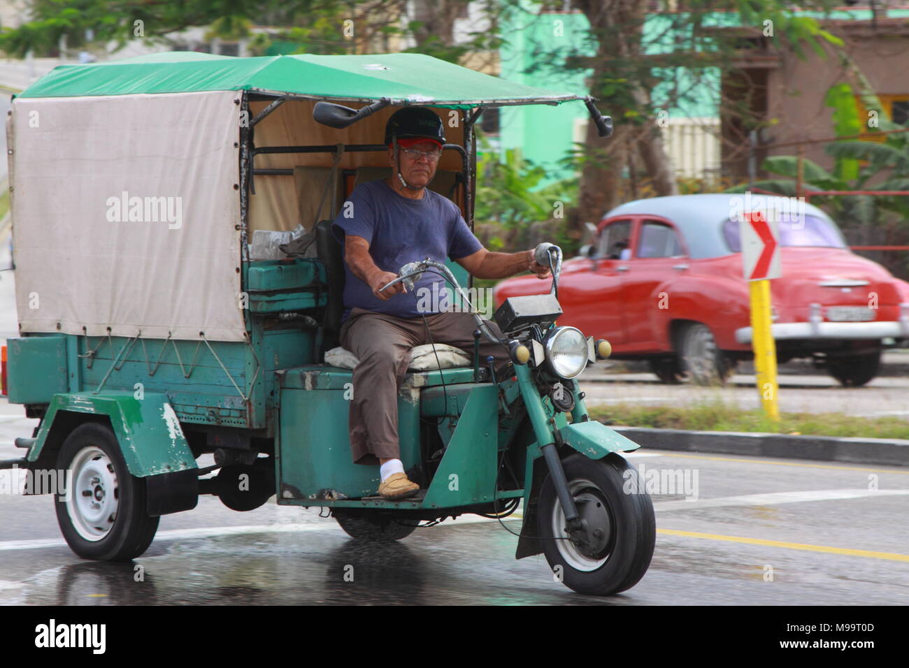 A man in blue T-shirt drives his old green tricycle cargo bike on the street of Havana, Cuba. Stock Photo