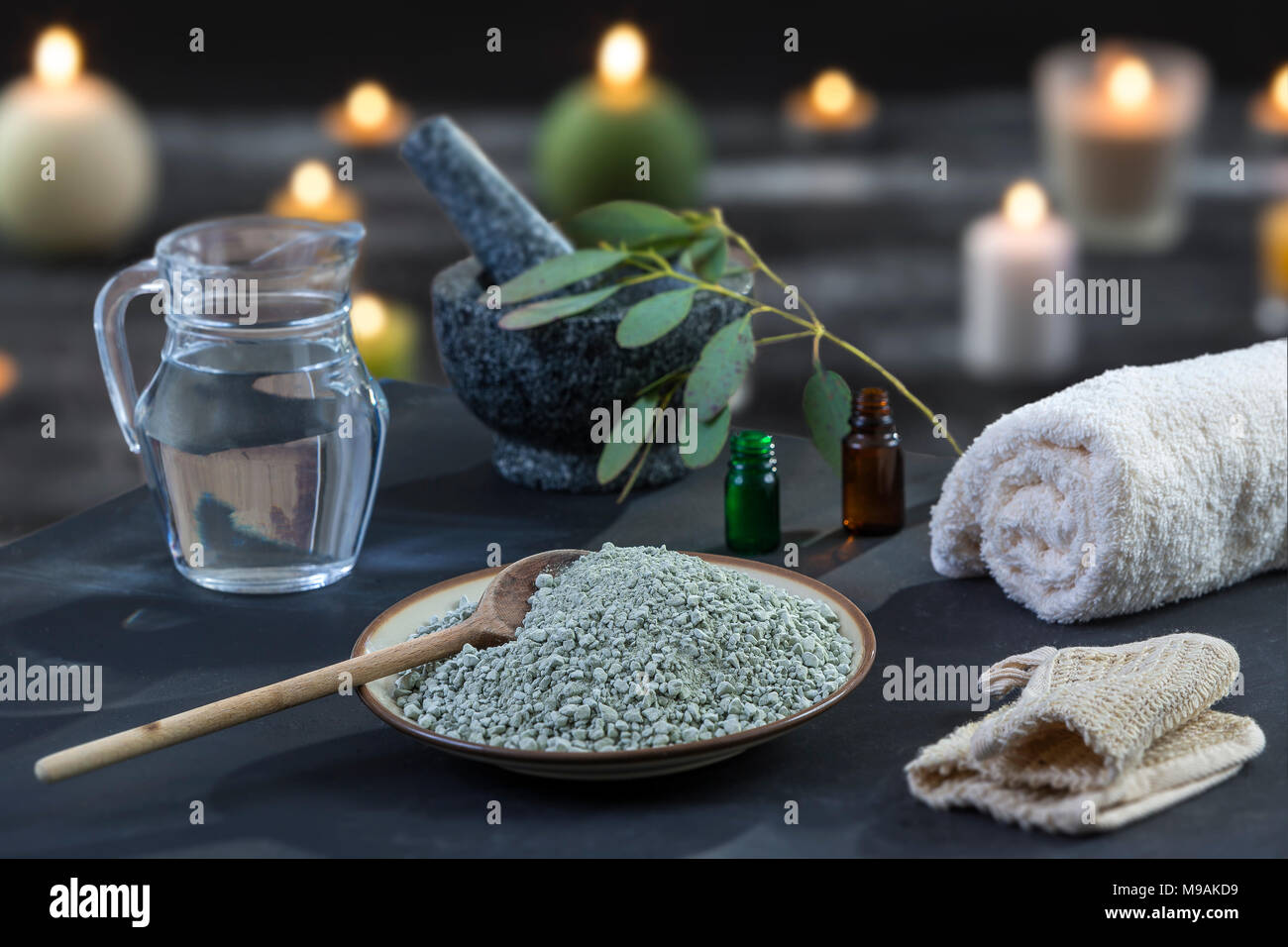 Spa composition on black wooden background. white rolled towels, alight candles, green herbs, eucalyptus clay mask for face and body, Stock Photo