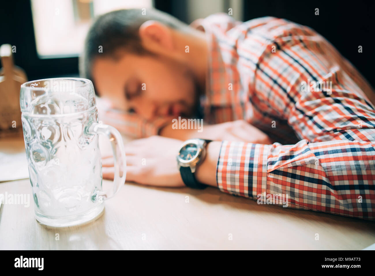 Drunk male customer leaning at the bar counter and sleeping while glass with beer standing near him Stock Photo
