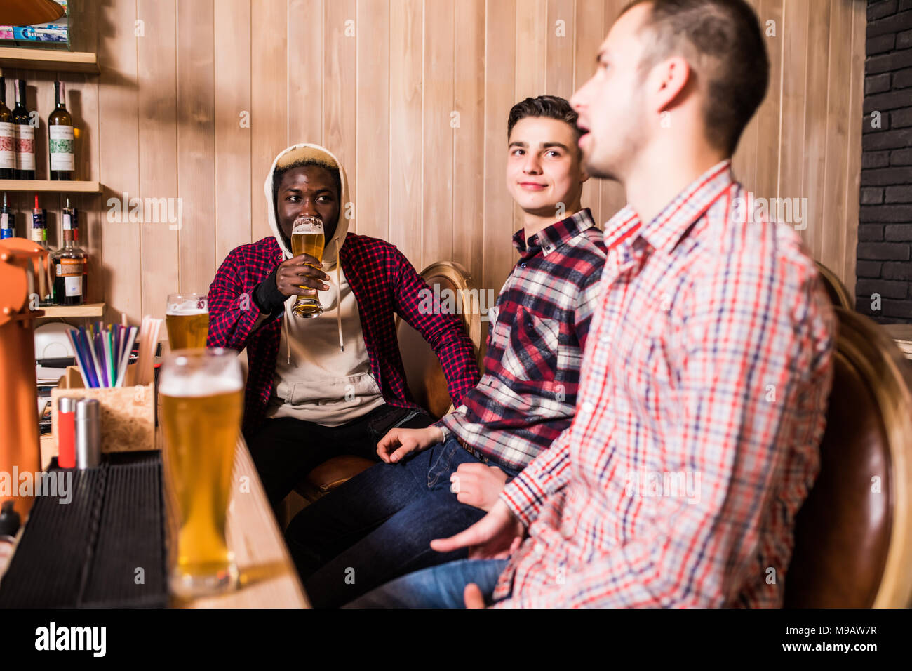 Three young men in casual clothes are smiling drinking beer while ...