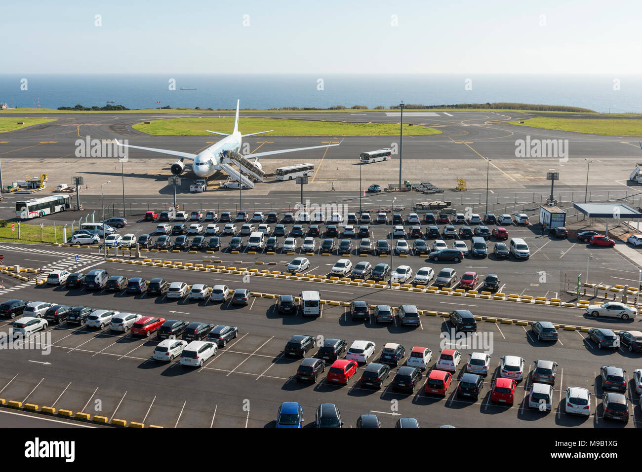 Aerial view on typical airport parking at São Miguels João Paulo II Airport, with the parking lot in the foreground and an airplane boarding in the ba Stock Photo