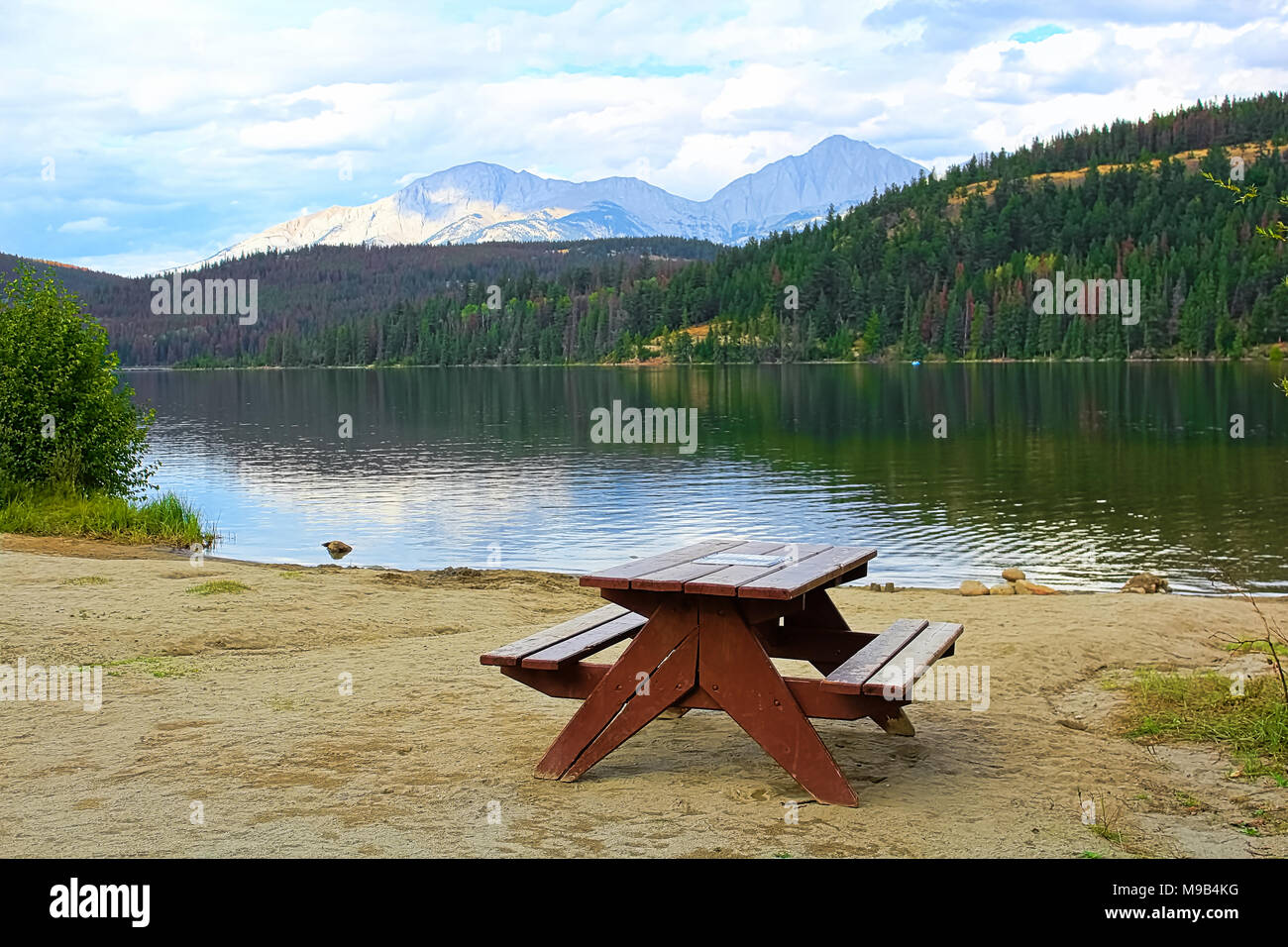 An empty picnic table on the edge of a mountain lake Stock Photo