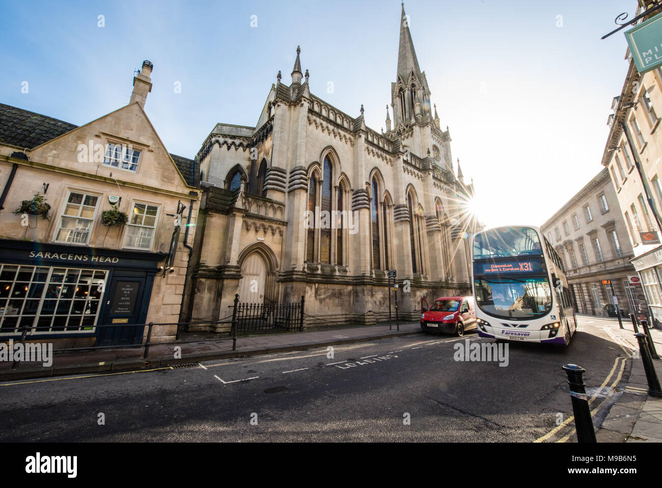 A First bus heads out of historic Broad Street in Bath with a red van in an empty car-free street with St Michael Without Church and the Saracens Head Stock Photo