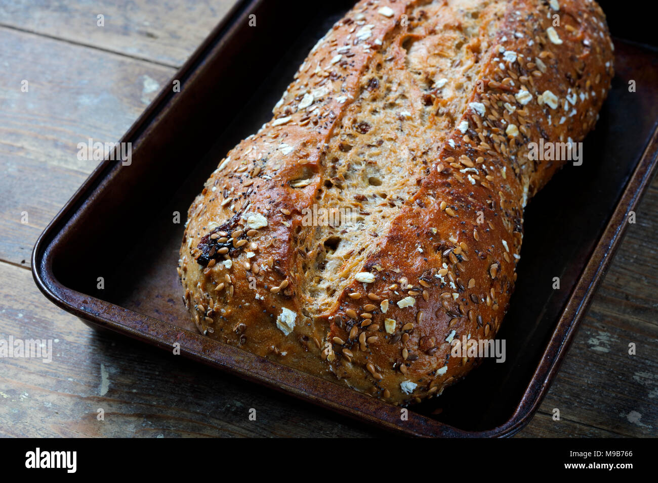 Rustic whole grain bread loaf in baking tray on wooden table Stock ...