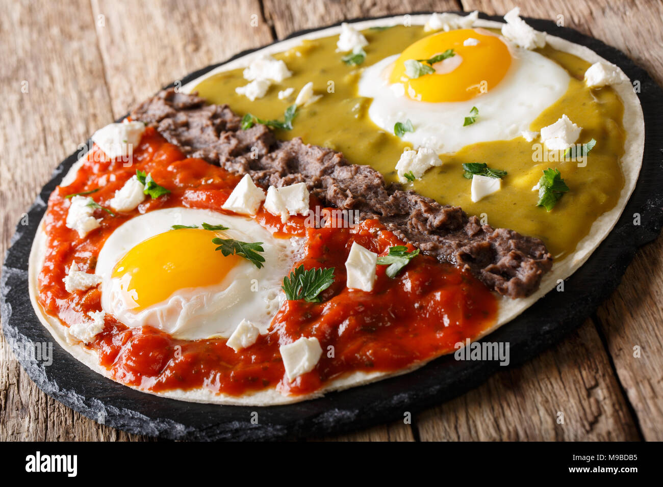 Mexican breakfast huevos divorciados of eggs with Frijoles refritos, sauces roja and verde and cheese Queso Fresco on a corn tortilla close-up on the  Stock Photo
