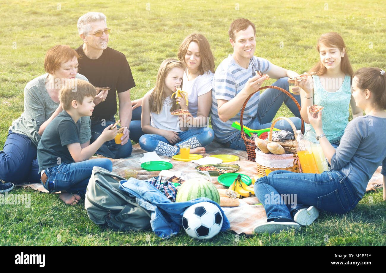 Friendly and smiling family with  kids talking and eating pizza at picnic in park Stock Photo