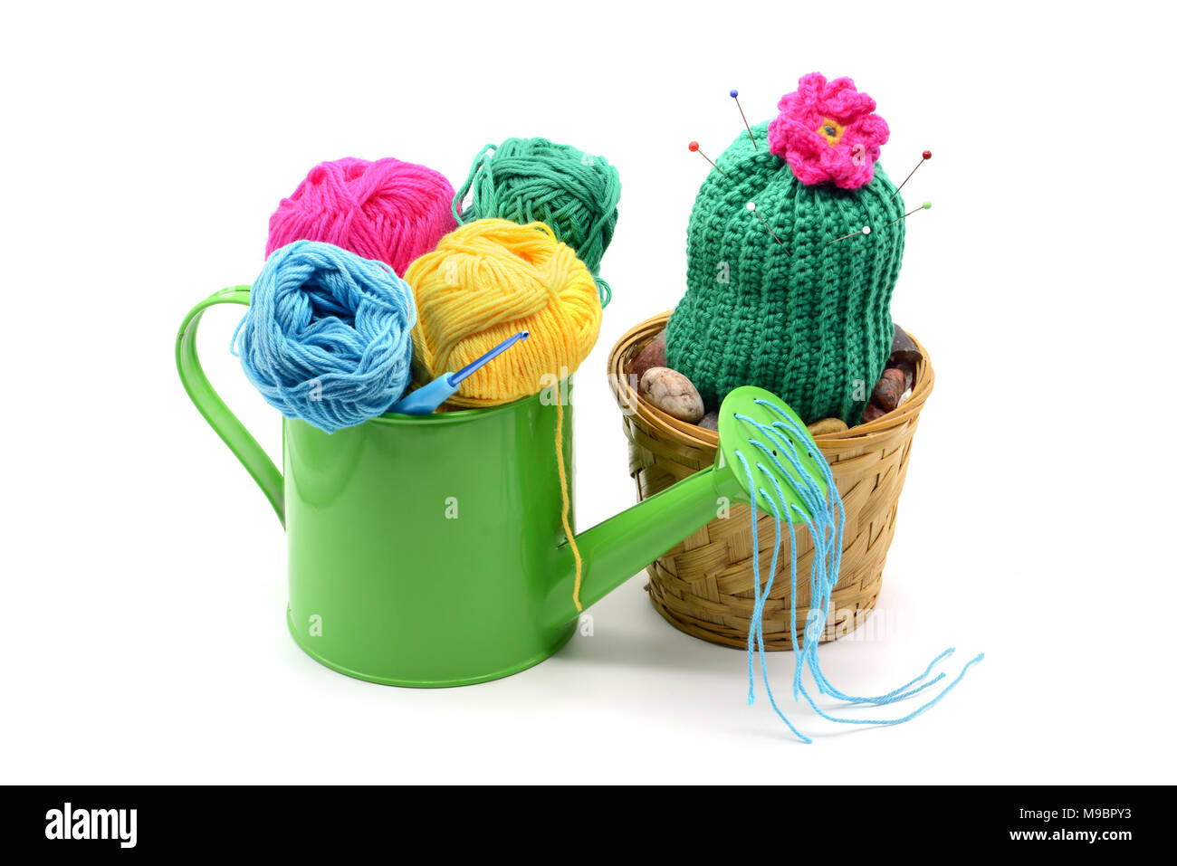 crochet cactus plant with flower head in flowerpot as pincushion. water can with wool balls in front. Stock Photo