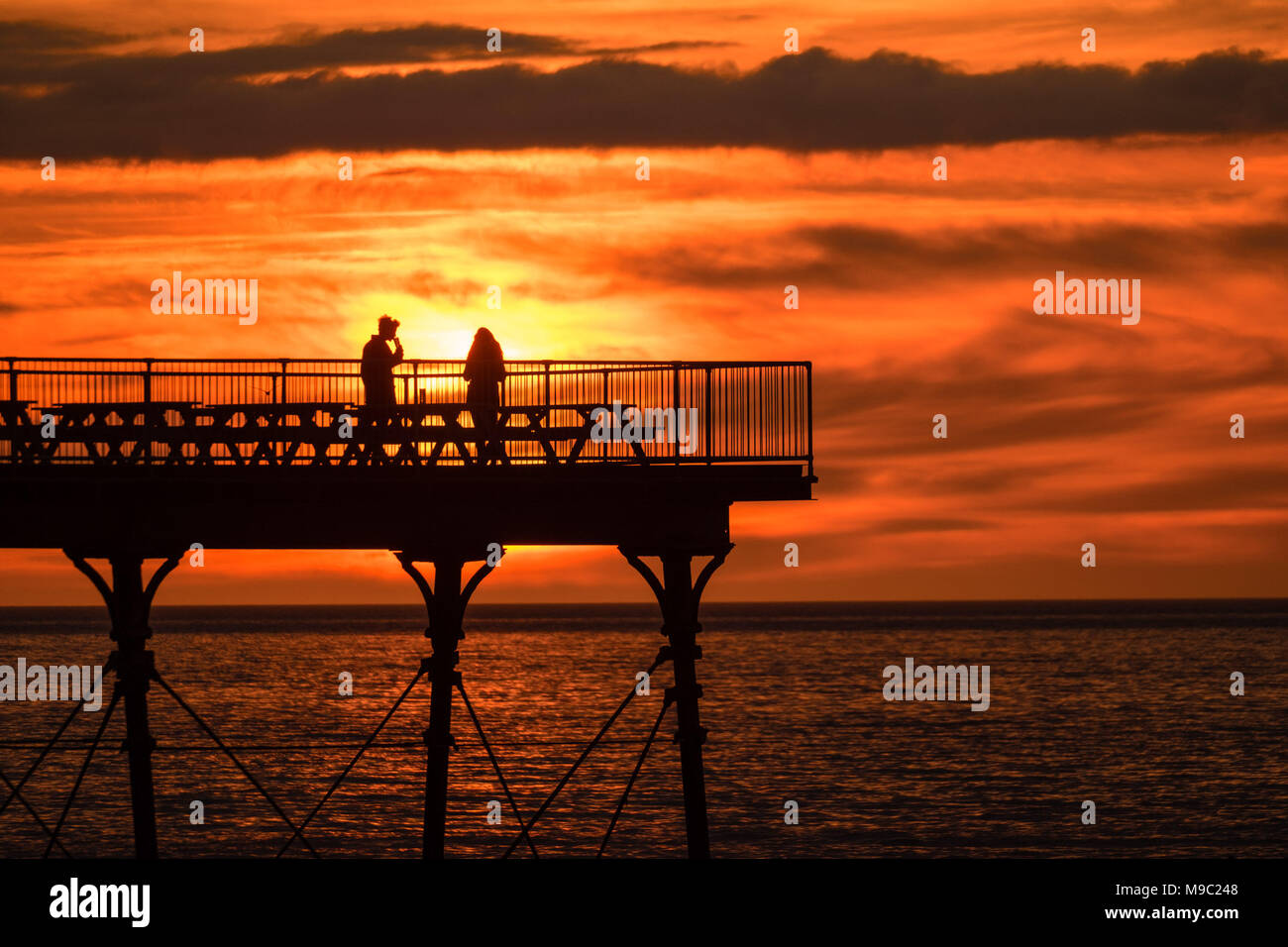 Aberystwyth Wales UK, Saturday 24 March 2018  UK Weather: People are silhouetted standing on the end of Aberystwyth pier  as the sun sets spectacularly over  Cardigan Bay ,  on the eve of British Summer Time, when the clocks go forwards and hour tonight  photo © Keith Morris  / Alamy Live News Stock Photo