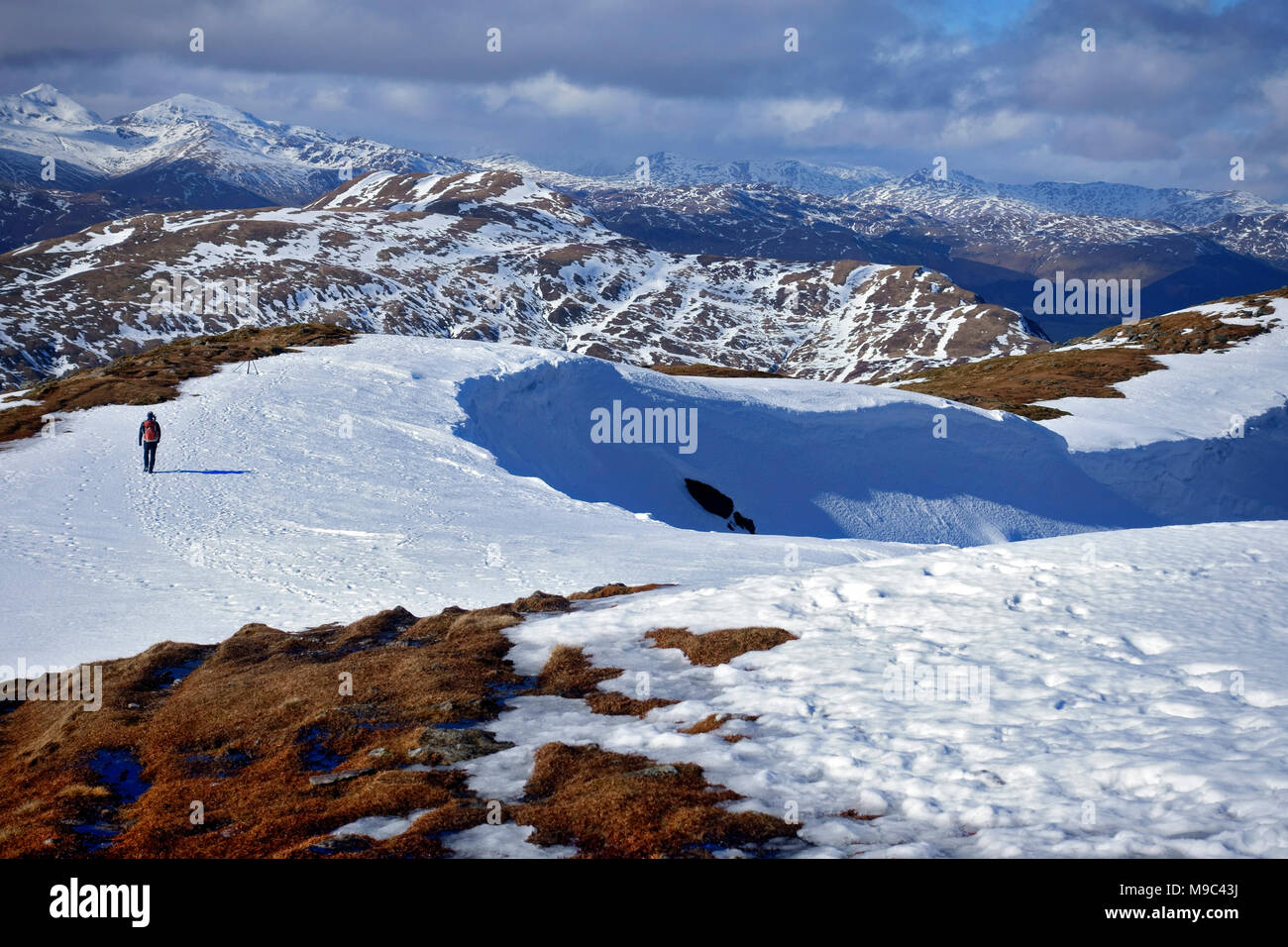 Hill walker starts the descent from the summit of Ben Ledi in the snow tracks of other recent