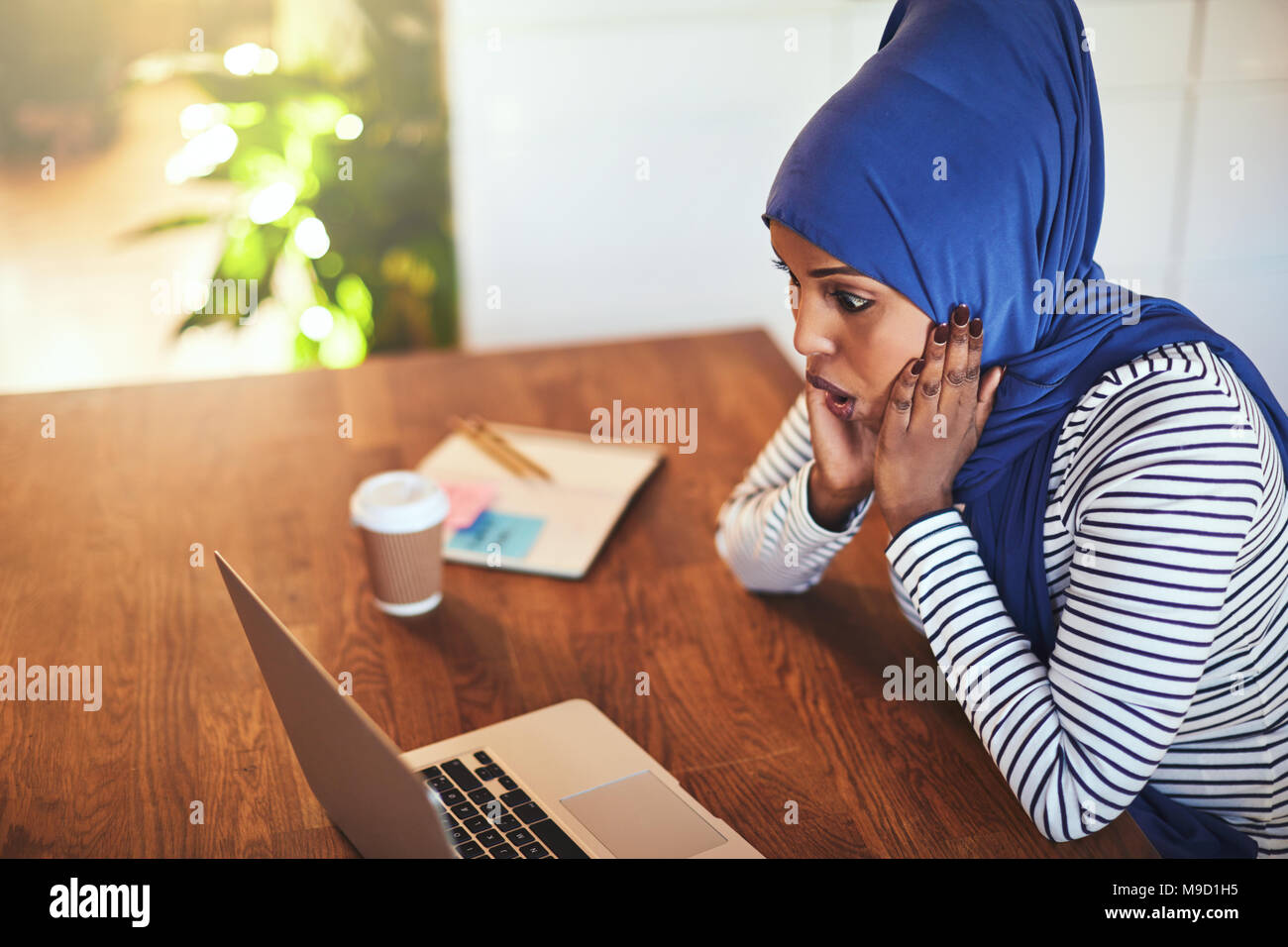 Young Arabic female entrepreneur wearing a hijab sitting at her kitchen ...