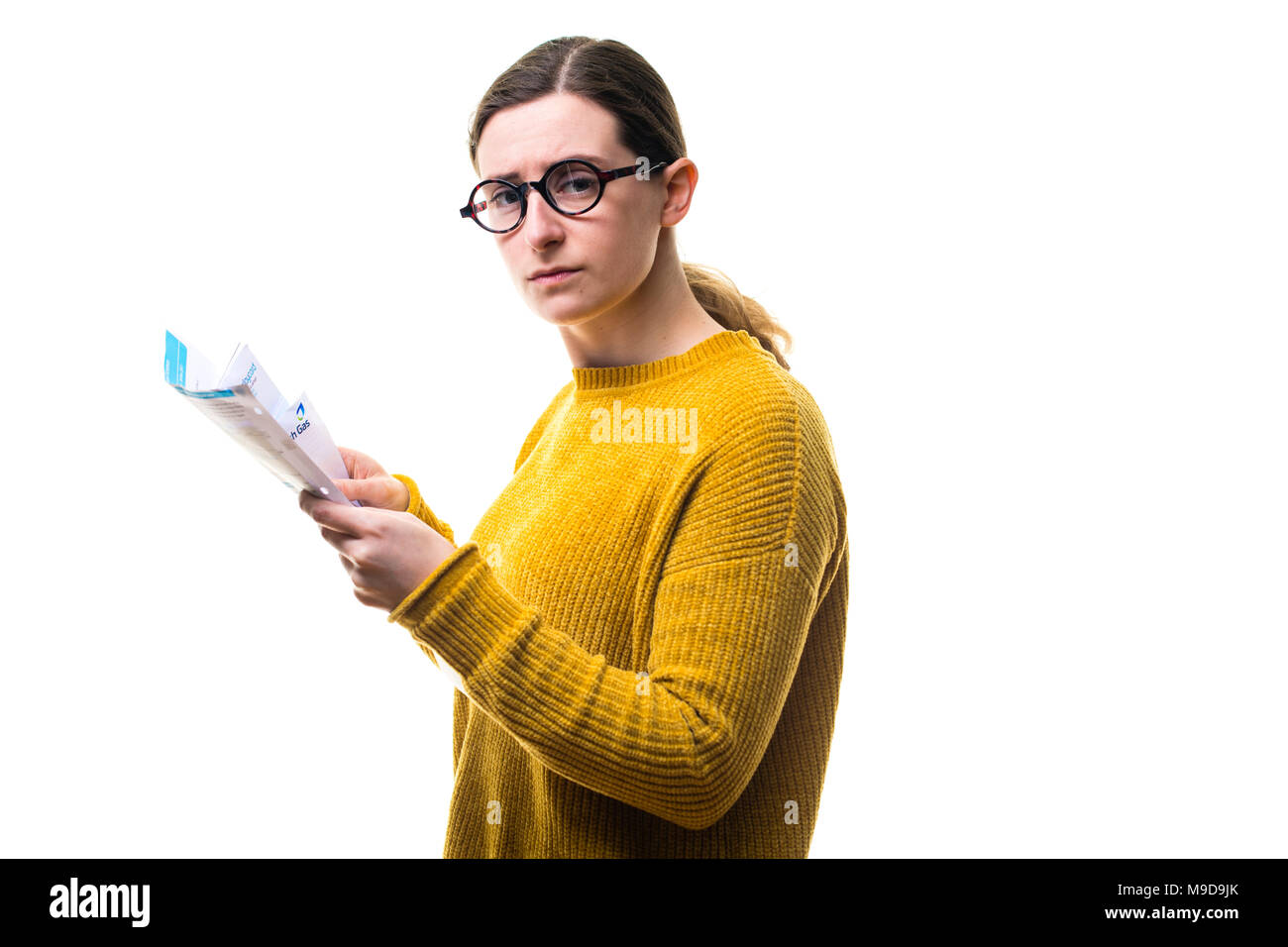 Money Worries and personal finances : A young Caucasian woman girl wearing a yellow jumper sweater, looking at her bills and worried about paying home domestic utility power charges , UK Stock Photo